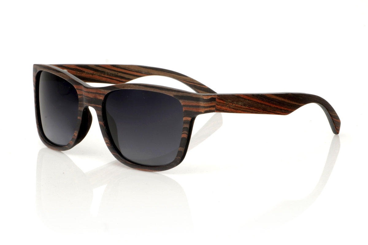 Wood eyewear of Ebony modelo ELEGANCE. ELEGANCE wooden sunglasses stand out for their less angular frame, designed to fit wider faces or for those who prefer oversized glasses. This model is characterized by its unique construction, with laminated ebony wood on the exterior and interior and sheets of maple wood interspersed on the contravein, and by the detail of the curvature of the frame in the grip to the temples, offering not only an effect Impressive visual but also a robust structure. With generous measurements of 155x50mm and a caliber of 55, these glasses are the perfect choice for those looking to combine comfort with a bold and elegant style. | Root Sunglasses® 